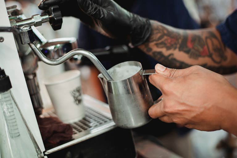 Crop faceless barista frothing milk with steam wand