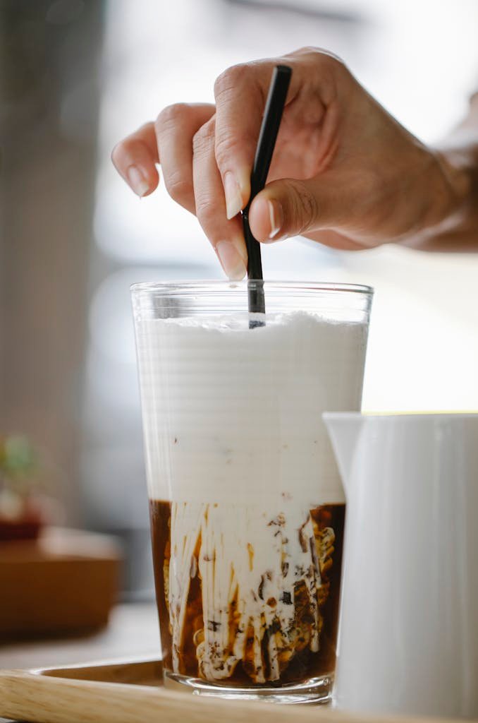 Crop faceless woman stirring iced latte with straw