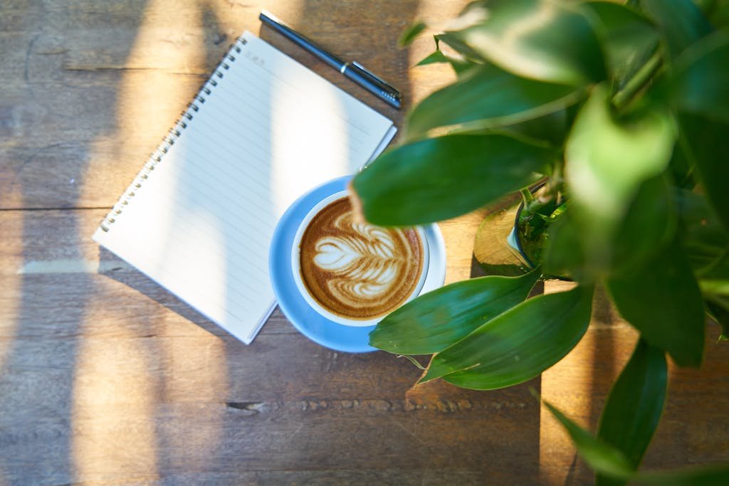 Cup of Latte Beside Spiral Notebook With Black Pen